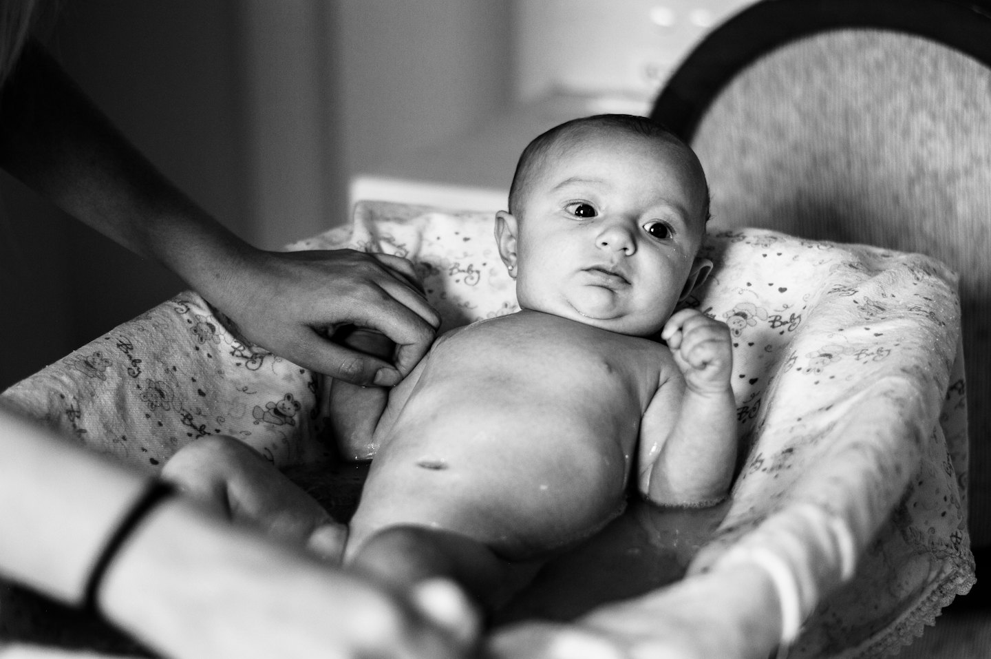 Erwachsene Hände baden vorsichtig ein Baby in einer Stoffliege.